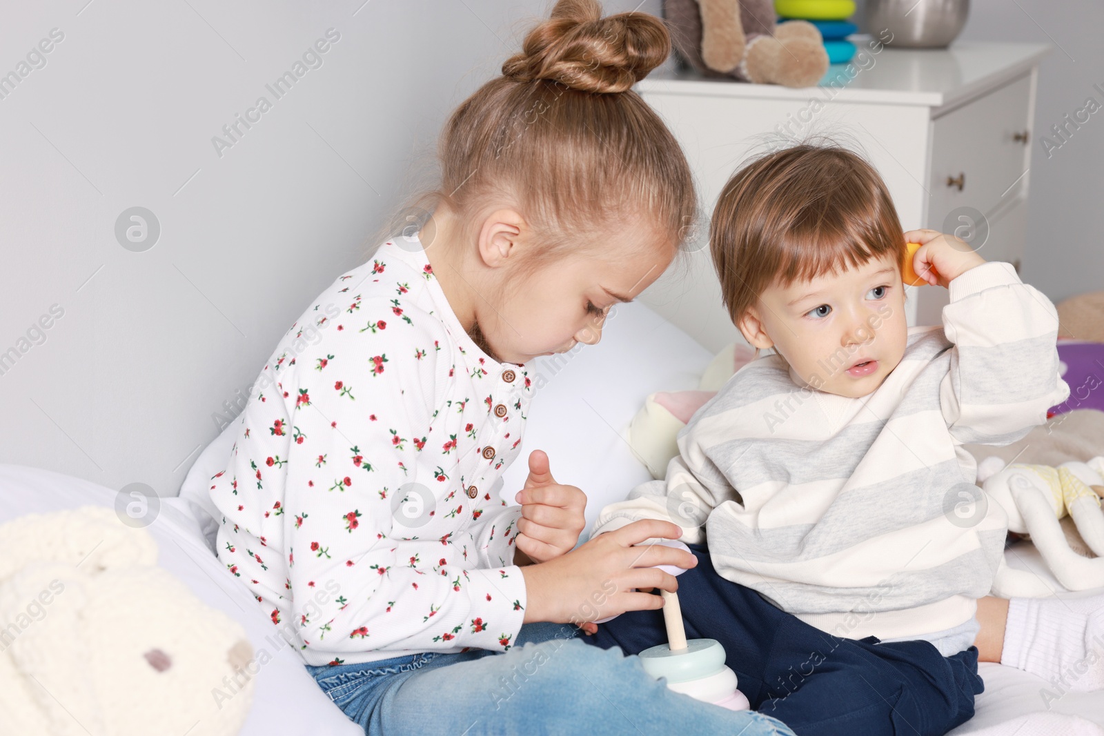 Photo of Sister and brother playing with toy pyramid on bed indoors