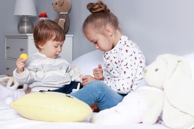 Photo of Sister and brother playing with toy pyramid on bed indoors