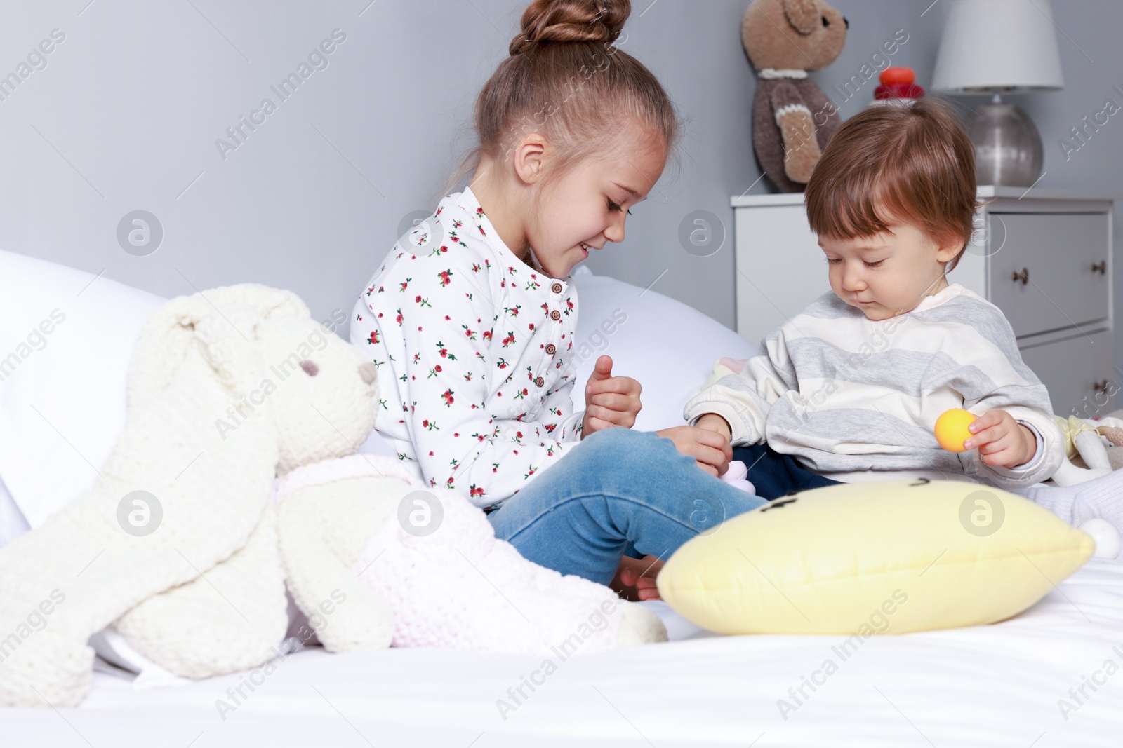 Photo of Sister and brother playing with toy pyramid on bed indoors