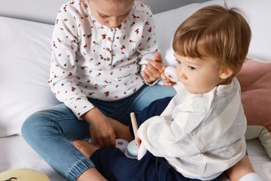 Photo of Sister and brother playing with toy pyramid on bed indoors