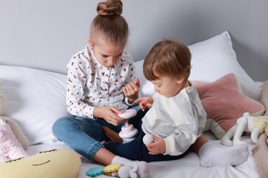 Photo of Sister and brother playing with toy pyramid on bed indoors