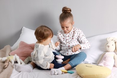 Sister and brother playing with toy pyramid on bed indoors