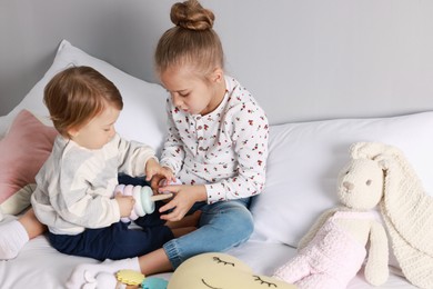 Photo of Sister and brother playing with toy pyramid on bed indoors