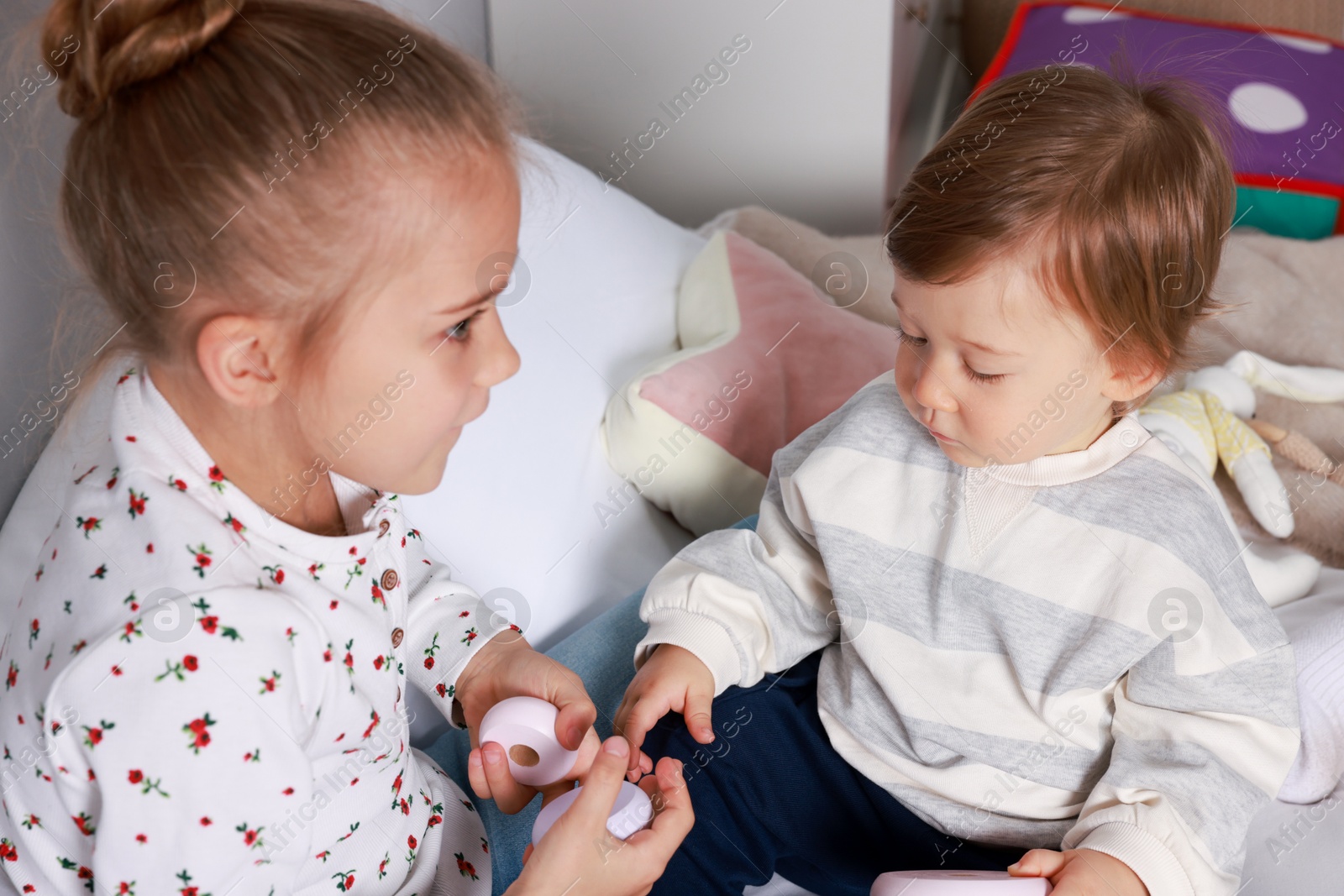 Photo of Sister and brother playing with toy pyramid on bed indoors