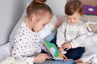 Photo of Sister and brother reading book together on bed indoors