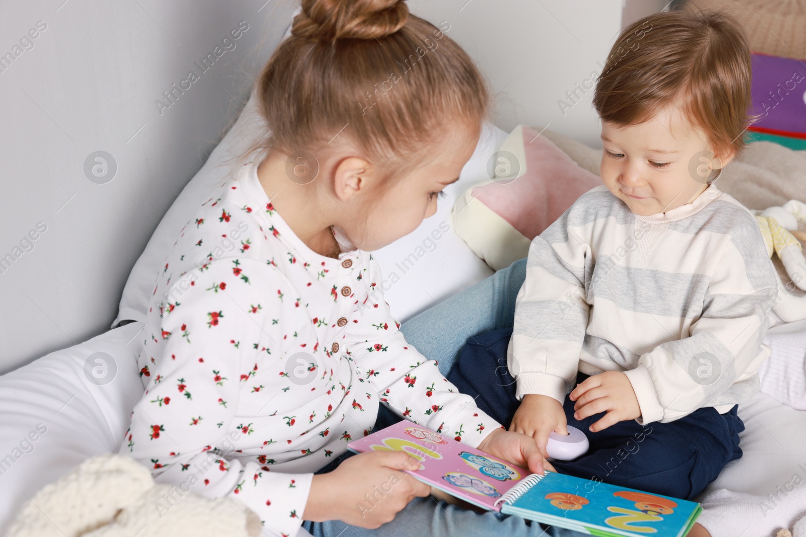 Photo of Sister and brother reading book together on bed indoors