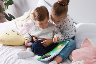 Photo of Sister and brother reading book together on bed indoors