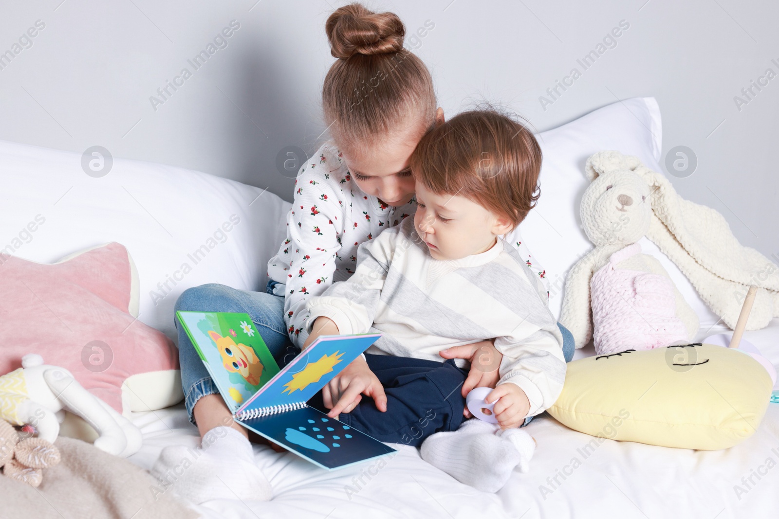 Photo of Sister and brother reading book together on bed indoors