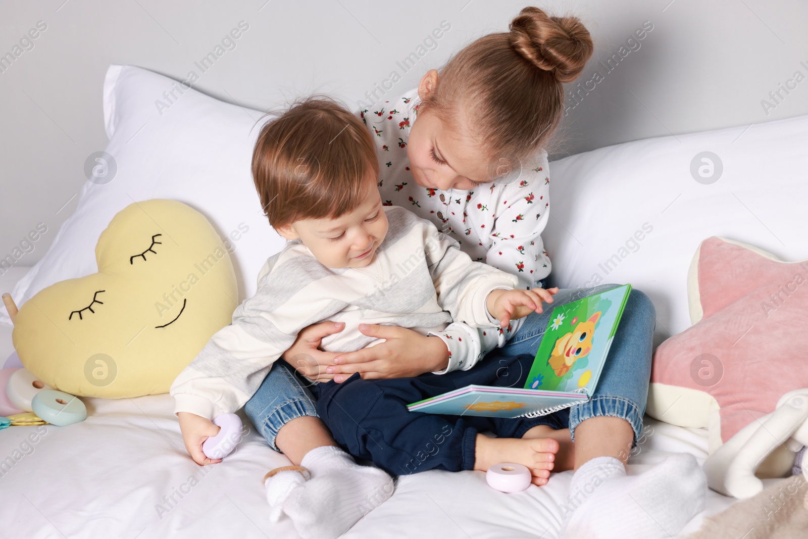 Photo of Sister and brother reading book together on bed indoors