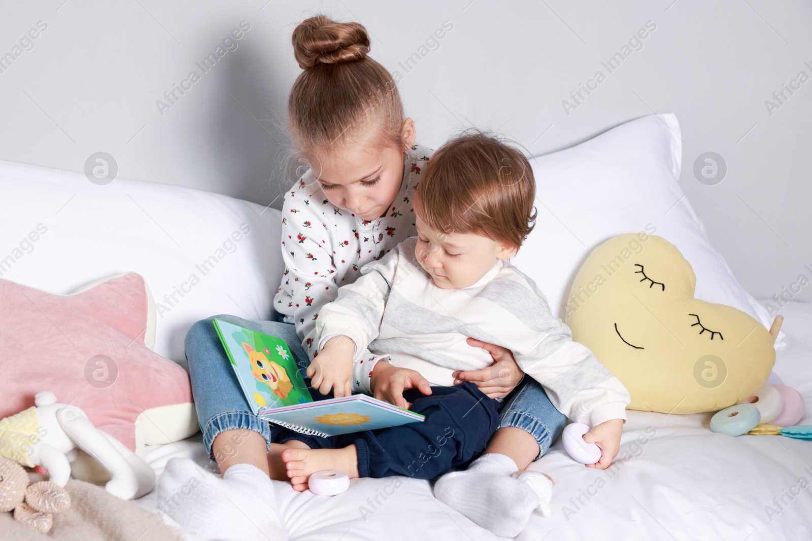 Photo of Sister and brother reading book together on bed indoors