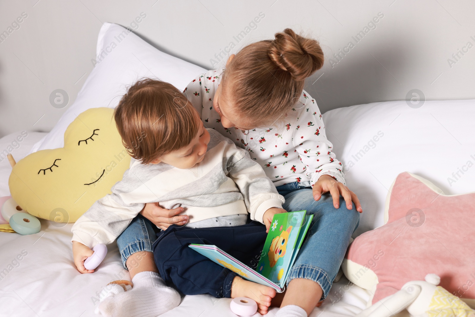 Photo of Sister and brother reading book together on bed indoors