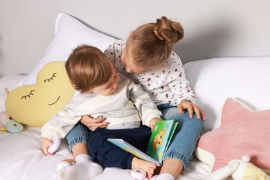 Photo of Sister and brother reading book together on bed indoors