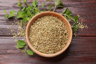 Photo of Dried oregano in bowl and green leaves on wooden table, top view