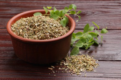 Photo of Dried oregano in bowl and green leaves on wooden table, closeup