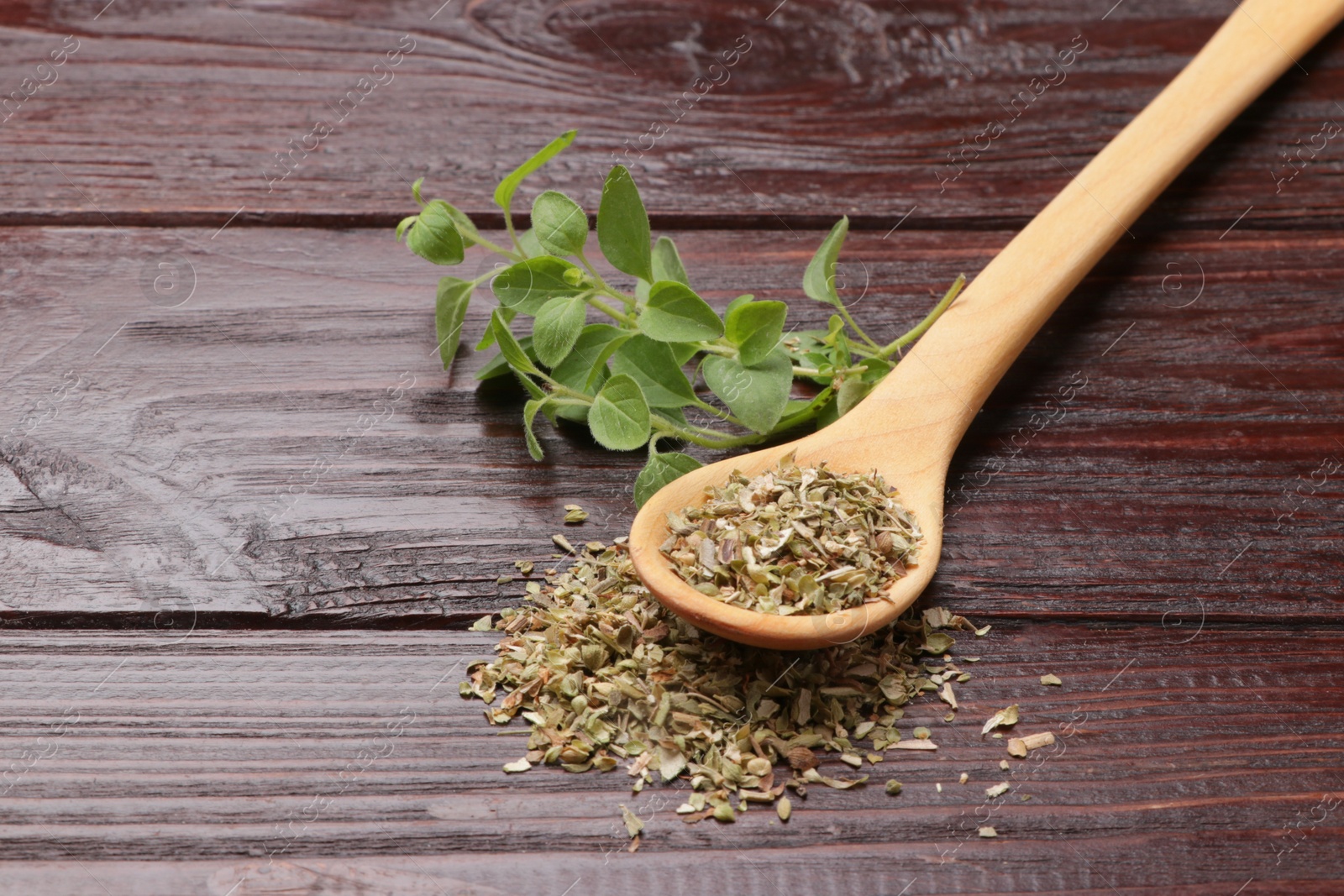 Photo of Dried oregano in spoon and green leaves on wooden table, closeup. Space for text