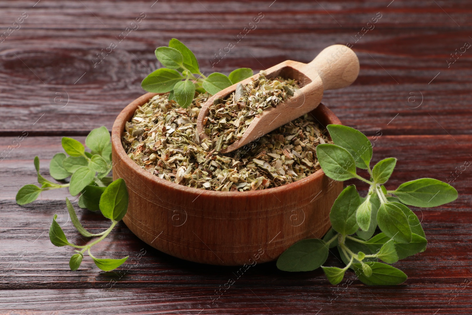 Photo of Dried oregano in bowl, scoop and green leaves on wooden table, closeup