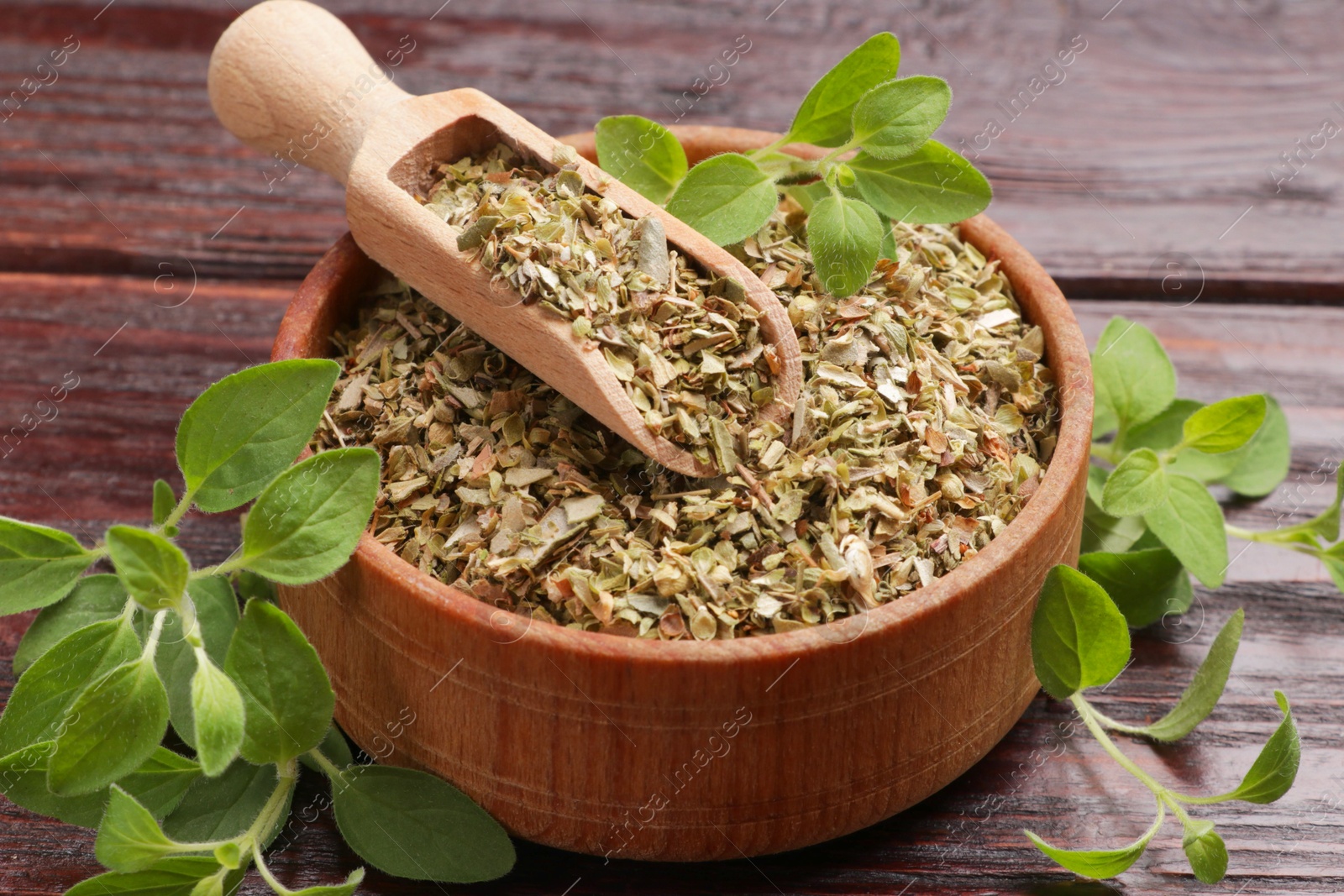 Photo of Dried oregano in bowl, scoop and green leaves on wooden table, closeup