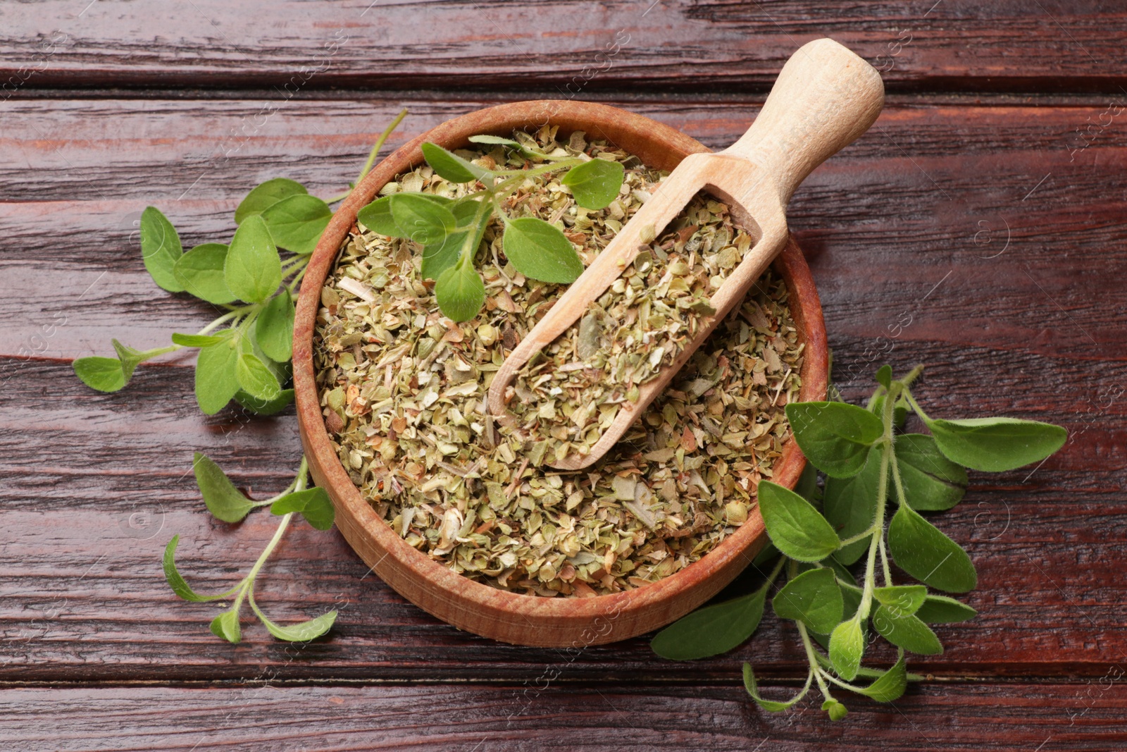 Photo of Dried oregano in bowl, scoop and green leaves on wooden table, top view