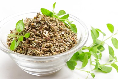 Photo of Dried oregano in glass bowl and green leaves on white table, closeup