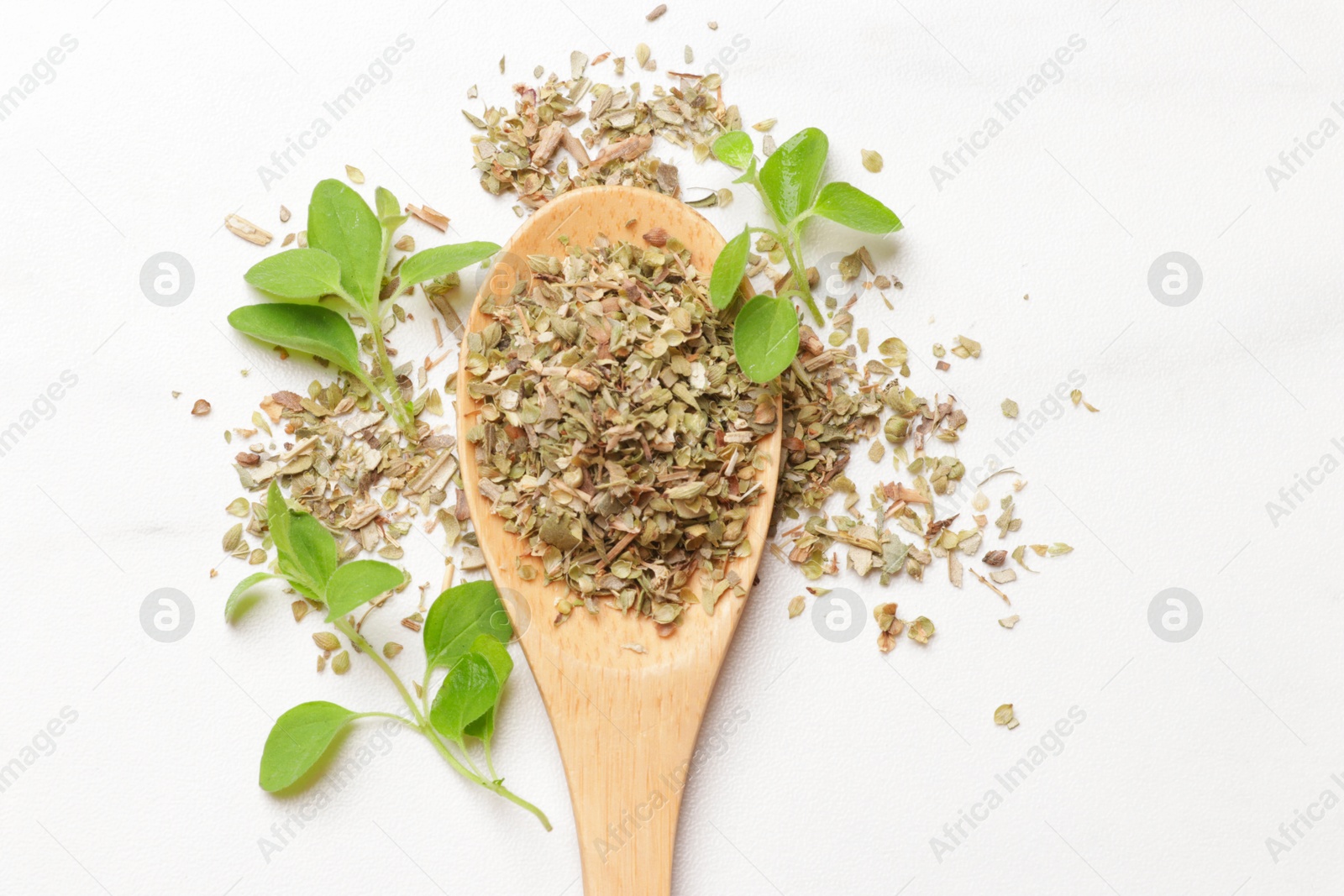 Photo of Dried oregano in wooden spoon and green leaves on white table, top view