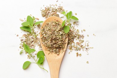 Photo of Dried oregano in wooden spoon and green leaves on white table, top view