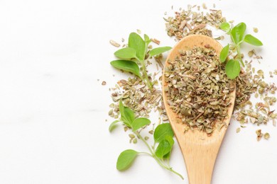 Dried oregano in wooden spoon and green leaves on white table, top view. Space for text