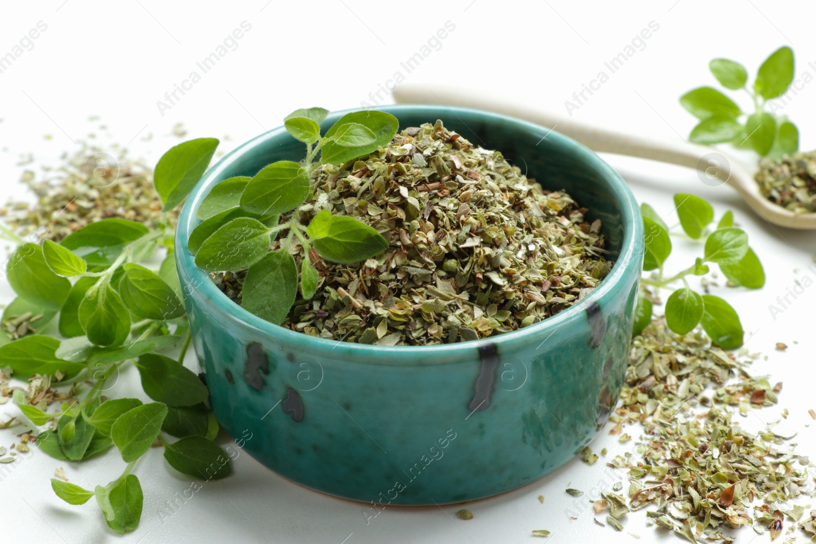 Photo of Dried oregano in bowl and green leaves on white table, closeup