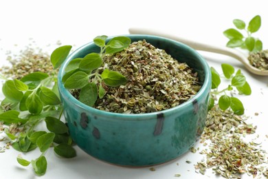 Photo of Dried oregano in bowl and green leaves on white table, closeup