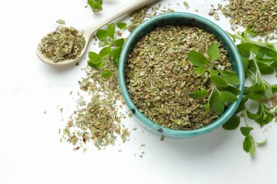 Photo of Dried oregano in bowl, spoon and green leaves on white table, top view