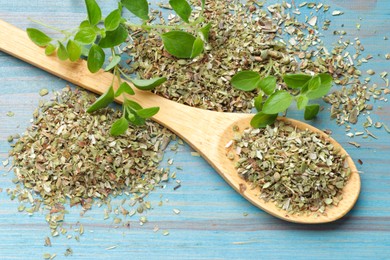 Dried oregano in spoon and green leaves on light blue wooden table, closeup