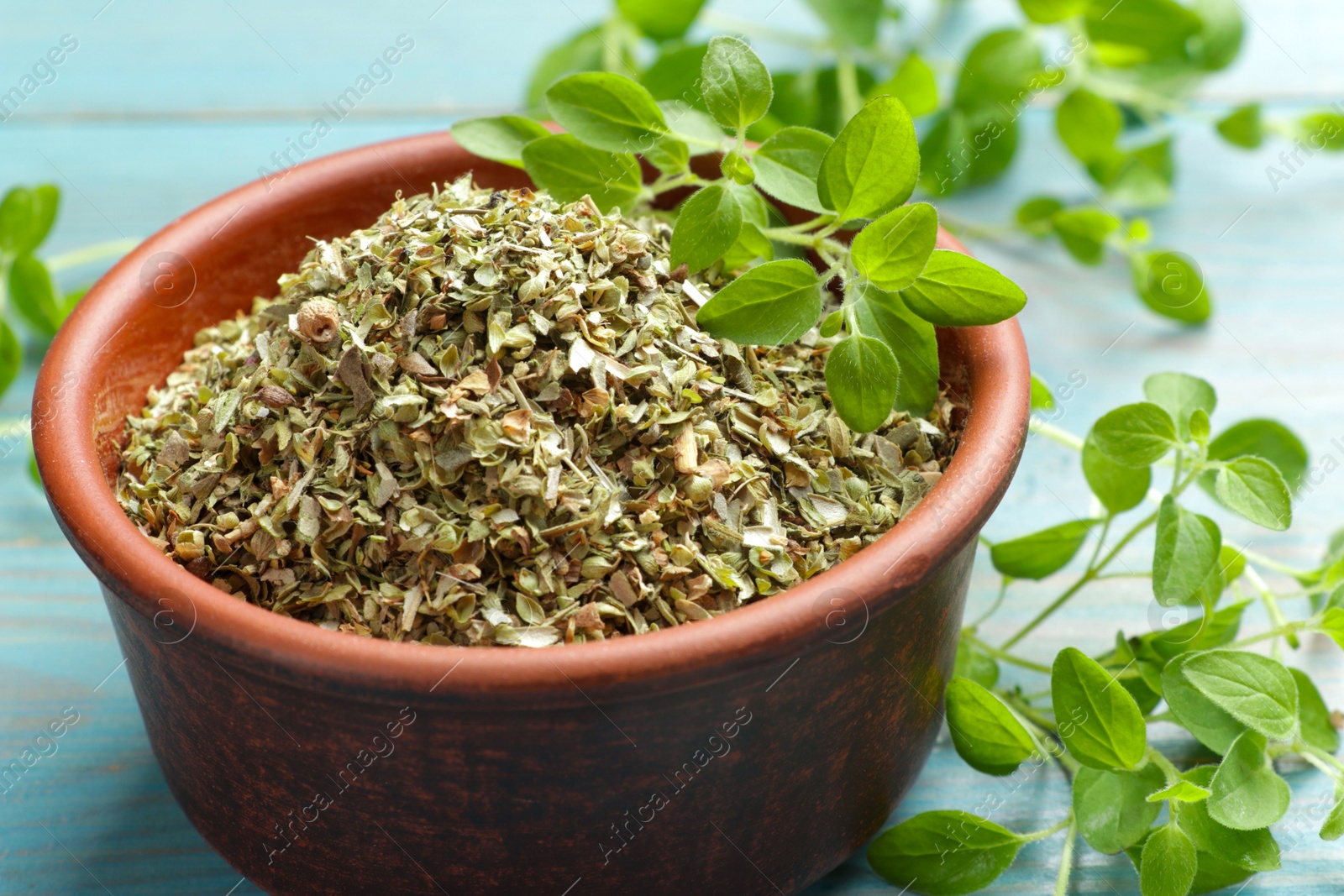 Photo of Dried oregano in bowl and green leaves on table, closeup