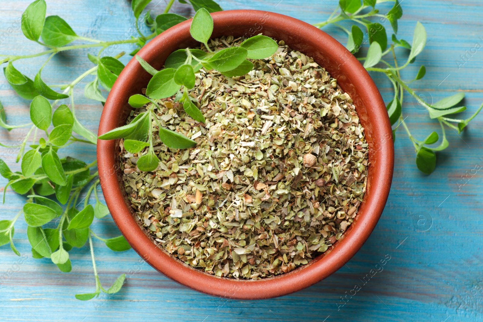 Photo of Dried oregano in bowl and green leaves on light blue wooden table, top view