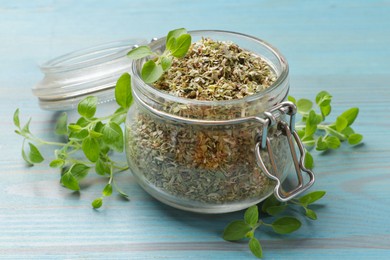 Photo of Dried oregano in glass jar and green leaves on light blue wooden table, closeup