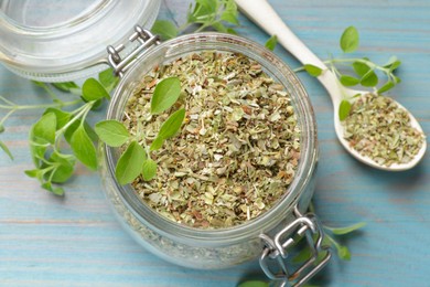 Photo of Dried oregano in glass jar, spoon and green leaves on light blue wooden table, above view