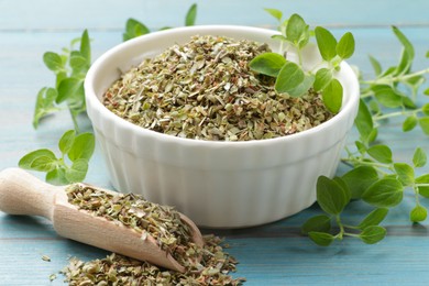 Photo of Dried oregano in bowl, scoop and green leaves on light blue wooden table, closeup