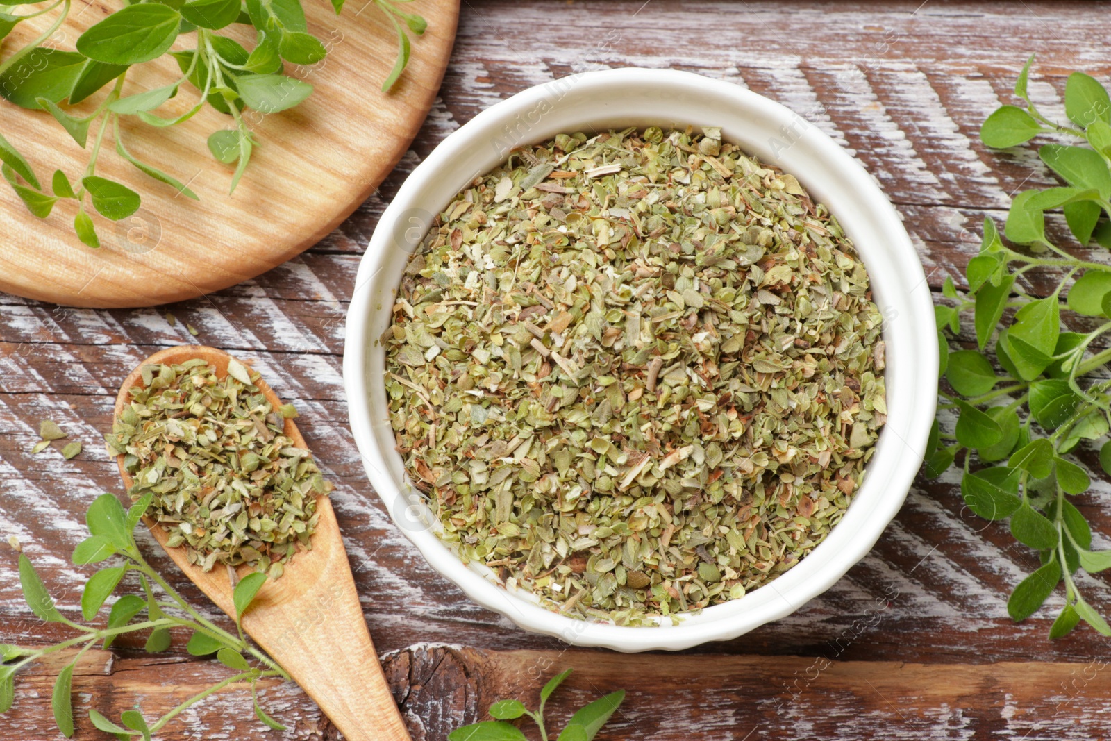 Photo of Dried oregano in bowl, spoon and green leaves on wooden table, top view