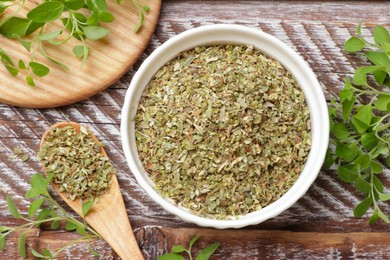 Photo of Dried oregano in bowl, spoon and green leaves on wooden table, top view