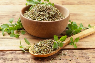 Photo of Dried oregano in bowl, spoon and green leaves on wooden table, closeup