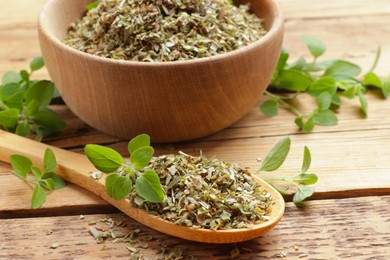 Photo of Dried oregano in bowl, spoon and green leaves on wooden table, closeup