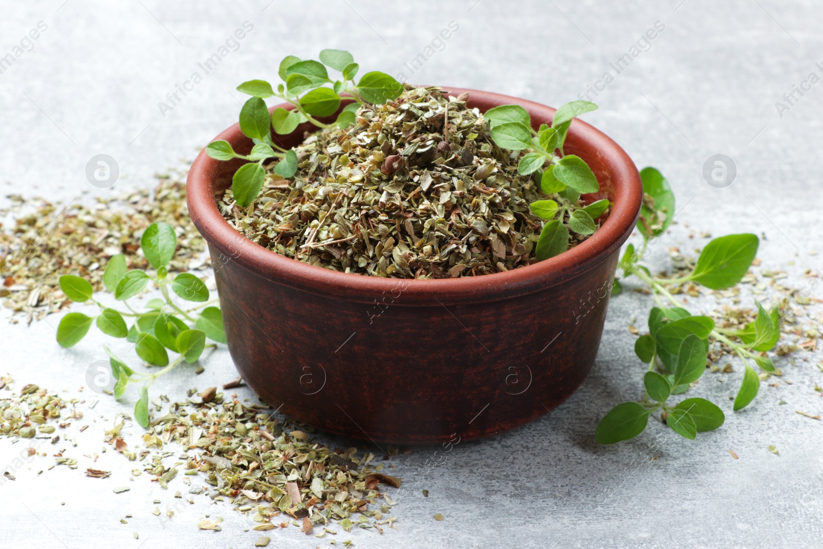 Photo of Dried oregano in bowl and green leaves on light grey table, closeup