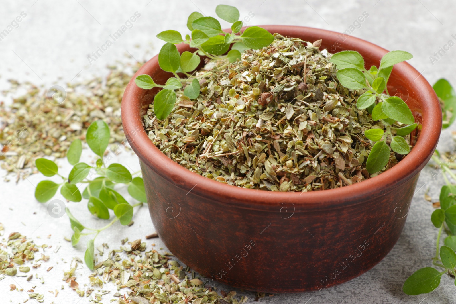 Photo of Dried oregano in bowl and green leaves on light grey table, closeup