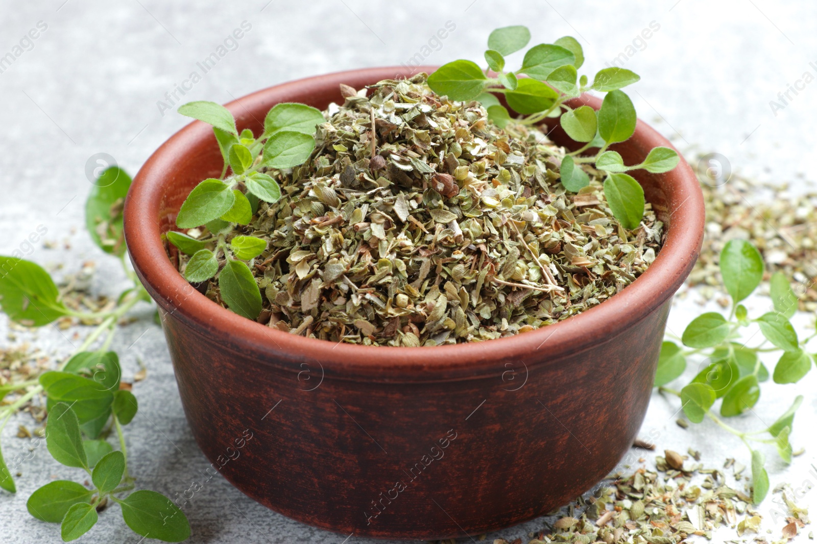 Photo of Dried oregano in bowl and green leaves on light grey table, closeup