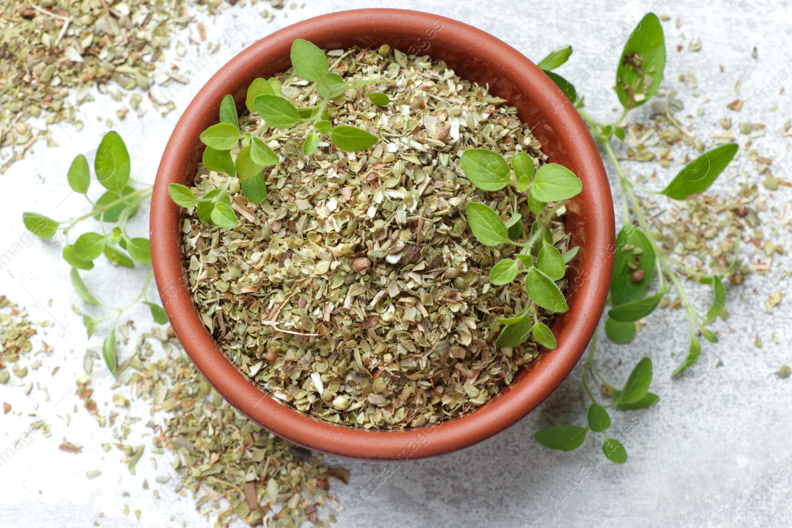 Photo of Dried oregano in bowl and green leaves on light grey table, top view