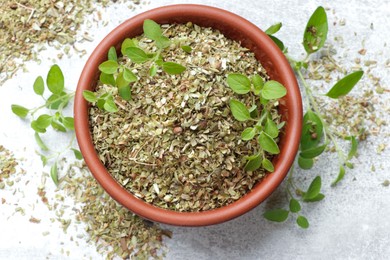 Photo of Dried oregano in bowl and green leaves on light grey table, top view