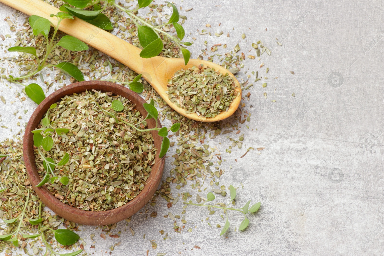 Photo of Dried oregano in bowl, spoon and green leaves on light grey table, top view. Space for text