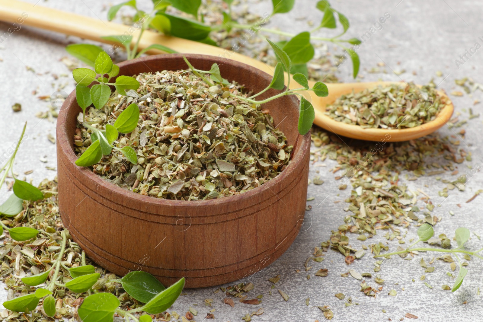 Photo of Dried oregano in bowl, spoon and green leaves on light grey table, closeup