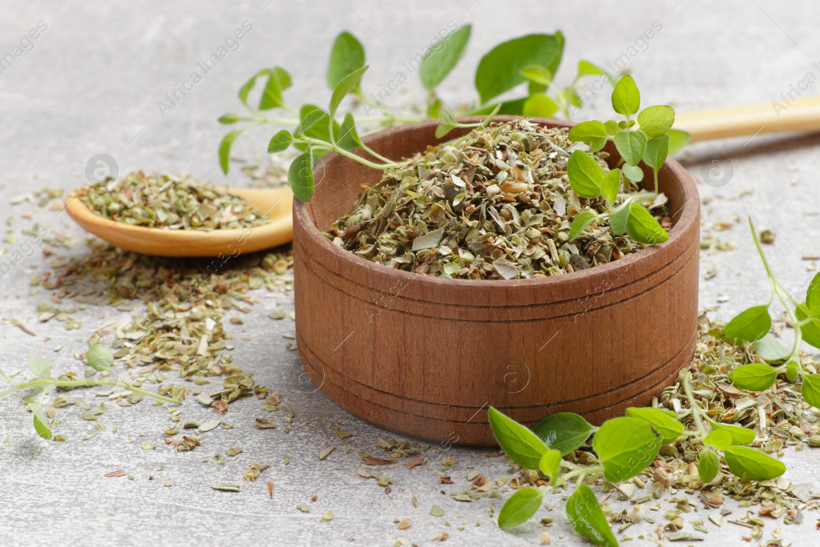 Photo of Dried oregano in bowl, spoon and green leaves on light grey table, closeup