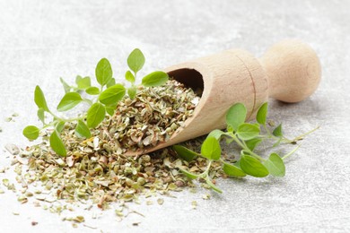 Dried oregano in scoop and green leaves on light grey table, closeup