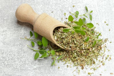 Dried oregano in scoop and green leaves on light grey table, top view