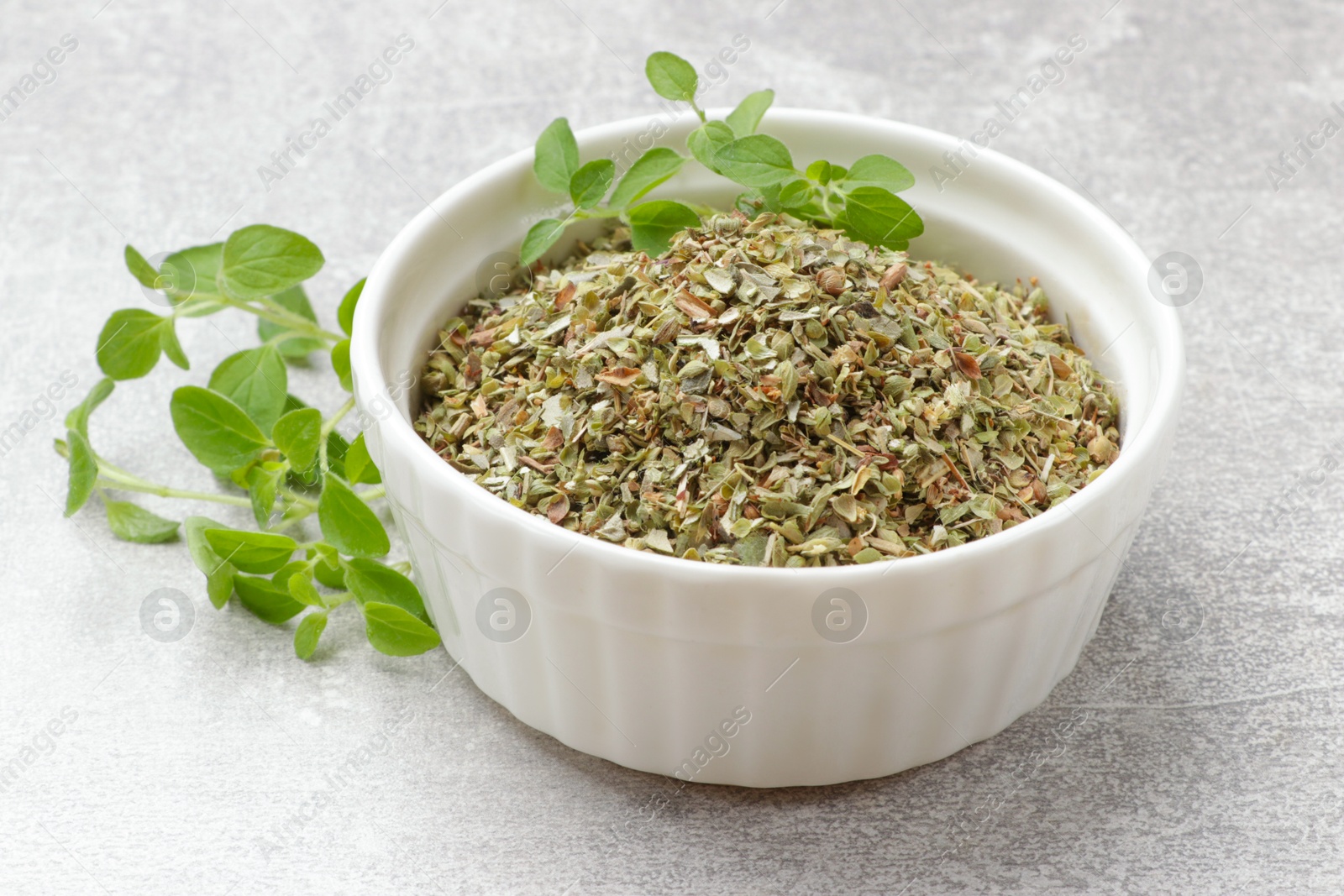 Photo of Dried oregano in bowl and green leaves on light grey table, closeup